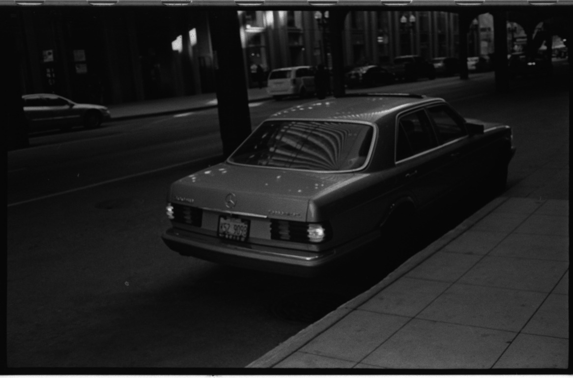 A parked Mercedes in the shadow of the elevated tracks.